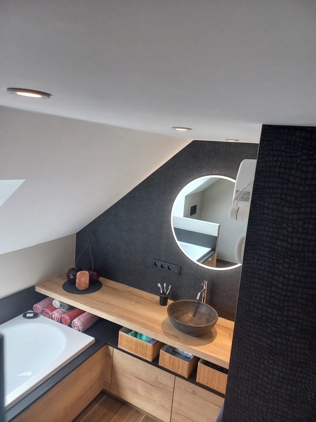 Mansardebadkamer met ronde verlichte spiegel en stenen wastafel